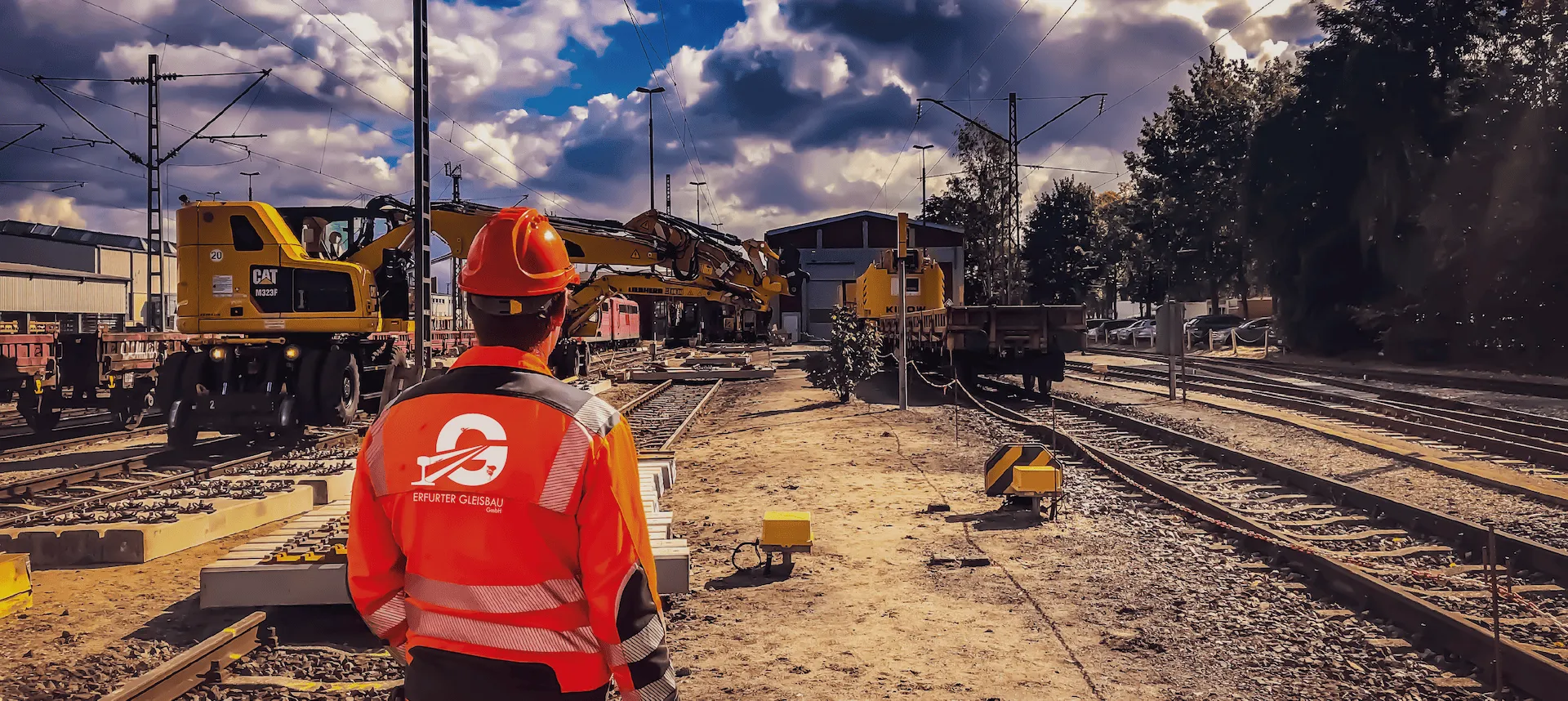 Mann steht auf Baustelle. Im Hintergrund ein Bagger auf dem Gleis.